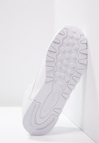 White athletic shoe sole with a textured surface, featuring circular and ridged patterns. Branding visible on the heel area.