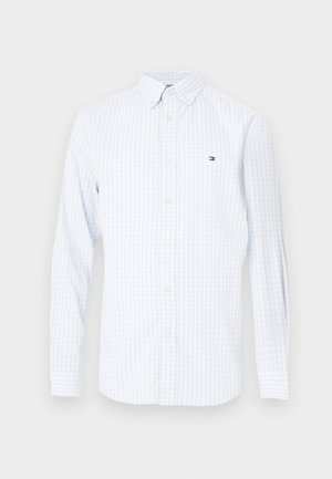 Langærmet hvid skjorte med lyseblå vertikale striber og et lille broderet flaglogo på brystet.