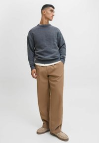 Gray knitted sweater with a round neck and ribbed cuffs, paired with beige wide-leg trousers and light brown slip-on shoes.