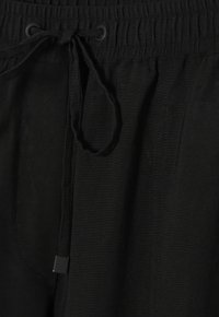 Zwarte joggers van ribbelstof, met een elastische tailleband, verstelbare trekkoord en zijzakken, voorzien van contrasterende stikseldetails.