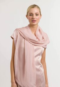 Hele roosa siidist sall on elegantseks tõmmatud kaela ümber, pehme tekstuur, voolav disain ja minimalistlik kuju, mis täiustab riietust.