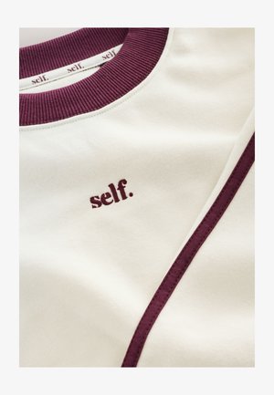 Cremefarbener Sweatshirt mit burgunderfarbenem Rippkragen, Seitenstreifen und dem Wort „self.“ in Burgunder auf der Brust bestickt.