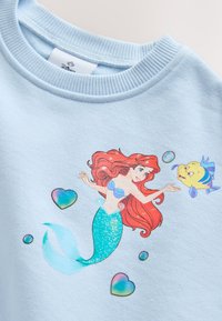 Sudadera azul claro con una ilustración de una sirena pelirroja y un pez amarillo rodeados de formas de corazón coloridas y burbujas.