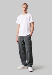 Witte katoen t-shirt met een klein logo, gecombineerd met grijze cargobroek met zijzakken en een label, aangevuld met witte sneakers.