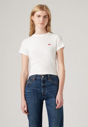 Camiseta blanca de manga corta ajustada con textura de canalé y un pequeño logo rojo de Levi's en el pecho izquierdo, combinada con jeans azules de cintura alta.