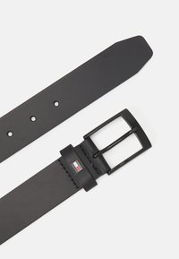 Cintura in pelle nera con estremità piatta, cinque fori di regolazione, una fibbia in metallo nero e un accento con logo vicino alla fibbia per la personalizzazione del marchio.