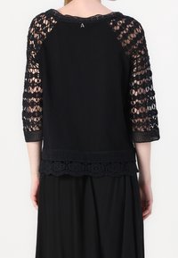 Top nero con maniche in pizzo a tre quarti e un orlo texturizzato con un motivo floreale all'uncinetto. Tessuto morbido con scollatura rotonda.