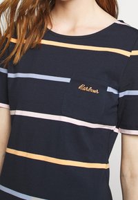 T-shirt w paski w odcieniach granatowym, pomarańczowym, różowym i jasnoniebieskim. Posiada małą kieszonkę na piersi oraz wyhaftowaną nazwę marki w kolorze pomarańczowym.