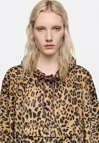 Sudadera con capucha de estampado de leopardo en tonos marrones y negros, con cuello ajustado con cordón y bolsillo delantero con cierre de presión.