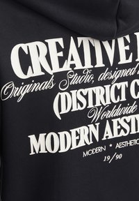 Navy hoodie featuring large white text with various fonts. Text includes "CREATIVE," "DISTRICT CO," and "MODERN AESTHETIC," with design details.