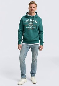 Türkiissinine dressipluus ees oleva kengurusahtli ning logoga ja tekstiga. Ühildub helesiniste teksade ja valgete tennistega.