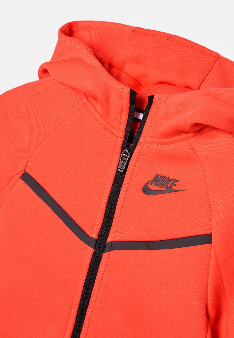 Czerwona bluza z kapturem z czarnym zamkiem błyskawicznym i akcentami. Posiada logo Nike na piersi, wykonana z miękkiego, teksturowanego materiału o dopasowanym kroju.