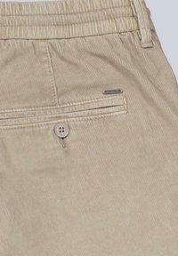 Beige Cordhosen mit einer Gesäßtasche, einem Knopfverschluss und einem kleinen Markenschild. Der Stoff hat eine gerippte Textur.