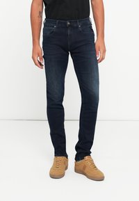 Mørkeblå slim-fit jeans lavet af denim, med et fem-lomme design og minimal falming, parret med brune sneakers.