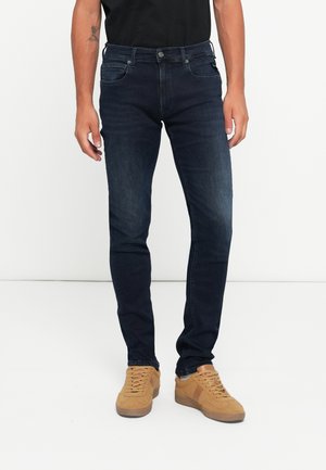 Mörkblå slim fit-jeans i denim, med femficksdesign och minimal blekning, matchat med tan sneakers.