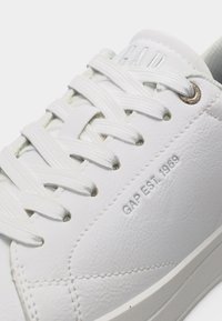 Baskets en cuir blanc avec lacets blancs, œillets métalliques et l'inscription "GAP EST. 1969" embossée sur le côté.