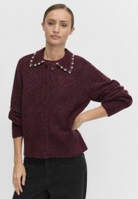 Burgundowa wełniana kardiganka z zapięciem na guziki, prą�żkowanymi mankietami i kołnierzem ozdobionym małymi, dekoracyjnymi perłami.