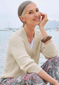Crème-kleurige gebreide cardigan met een v-hals, knoopsluiting en een gestructureerd patroon. Gecombineerd met broeken met paisleypatroon.