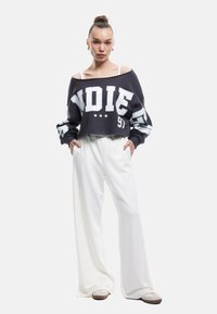 Przycięty czarny sweatshirt z białym napisem "INDIE", zestawiony z białymi spodniami o szerokich nogawkach z wysokim stanem. Miękka tkanina o luźnym kroju.
