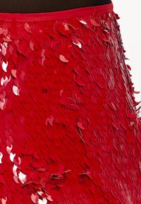 Jupe en sequins rouges ornée de sequins superposés en forme de feuilles avec une finition brillante. Ceinture lisse de couleur vive avec une surface texturée.
