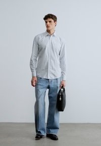 Vaaleanharmaa napillinen paita, haalistuneet leveälahkeiset farkut, musta nahkainen käsilaukku ja mustat kengät. Sileä kangas, jossa minimaalinen tekstuuri.