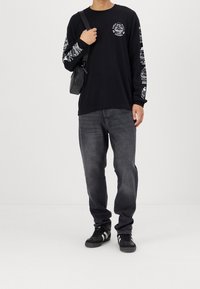 Maglietta nera a maniche lunghe con grafiche bianche sulle maniche, abbinata a jeans grigio scuro e sneakers nere. Piccola borsa a spalla nera.