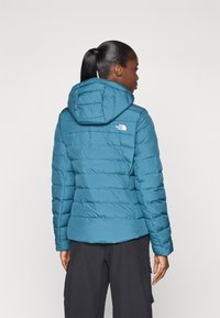 Blå puffjakke med hette, med quiltet design, frontlogo og lange ermer. Laget av lett og isolert materiale.
