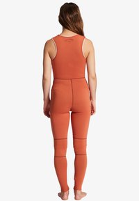 Verbrand oranje wetsuit met mouwloos ontwerp, flatlock naden en kniestukken. Gemaakt van rekbaar materiaal, aansluitend op het lichaam.