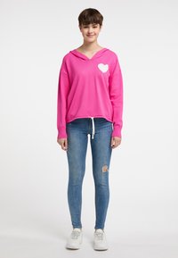 Felpa rosa brillante con scollatura a V e design di cuori bianchi, abbinata a jeans skinny blu e scarpe da ginnastica bianche. Tessuto morbido e vestibilità comoda.