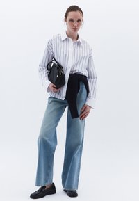 Camisa a rayas blancas, jeans de mezclilla azul claro, suéter azul marino atado a la cintura, bolso negro y mocasines negros. Tejido suave, corte relajado.