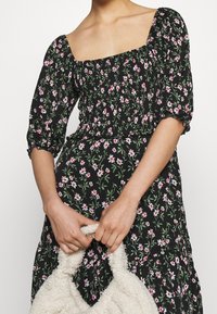 Schwarzes Blumenkleid mit kleinen pinken Blüten, quadratischem Ausschnitt, Puffärmeln und einem gestuften Rock, aus leichtem Stoff gefertigt.