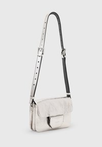 Silberne metallic Leder Umhängetasche mit Klappenverschluss, hexagonaler Hardware und einem zweifarbigen Trageriemen mit schwarzem Lederakzent.