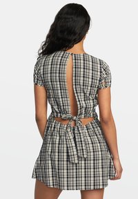 Zwart-wit geruite jurk met korte pofmouwen, open rug en striksluiting in de taille. Lichte stof met een gestructureerd patroon.