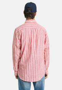 Rot-weiß gestreiftes Langarmhemd mit Button-Down-Kragen, ausgestattet mit einer Rückenfalte und abgerundetem Saum. Kombiniert mit blauen Jeans.
