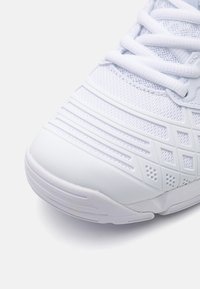 Scarpa da ginnastica bianca con tomaia in rete strutturata, suola in gomma e motivi geometrici sulla punta per una presa e uno stile migliorati.