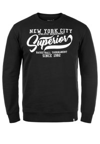 Czarna bluza z długimi rękawami, dekolt w kształcie litery U, z wyraźnym białym napisem: "NEW YORK CITY ATHLETIC DEPARTMENT SUPERIOR BASKETBALL TOURNAMENT SINCE 1982."