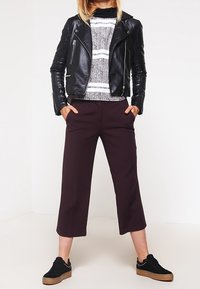 Svart läderbikerjacka, grå randig tröja, mörkbordeaux korta byxor och svarta sneakers med en texturerad sula och nitar.