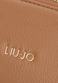 Portafoglio in pelle tan con superficie textured e logo "LIU:JO" in rilievo color oro. Chiusura con zip e dettagli di cucitura liscia.
