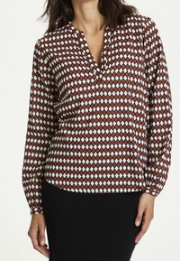 Blusa a maniche lunghe con motivo a rombi rossi e bianchi, dotata di scollatura a V e vestibilità rilassata. Tessuto leggero e morbido con una leggera lucentezza.