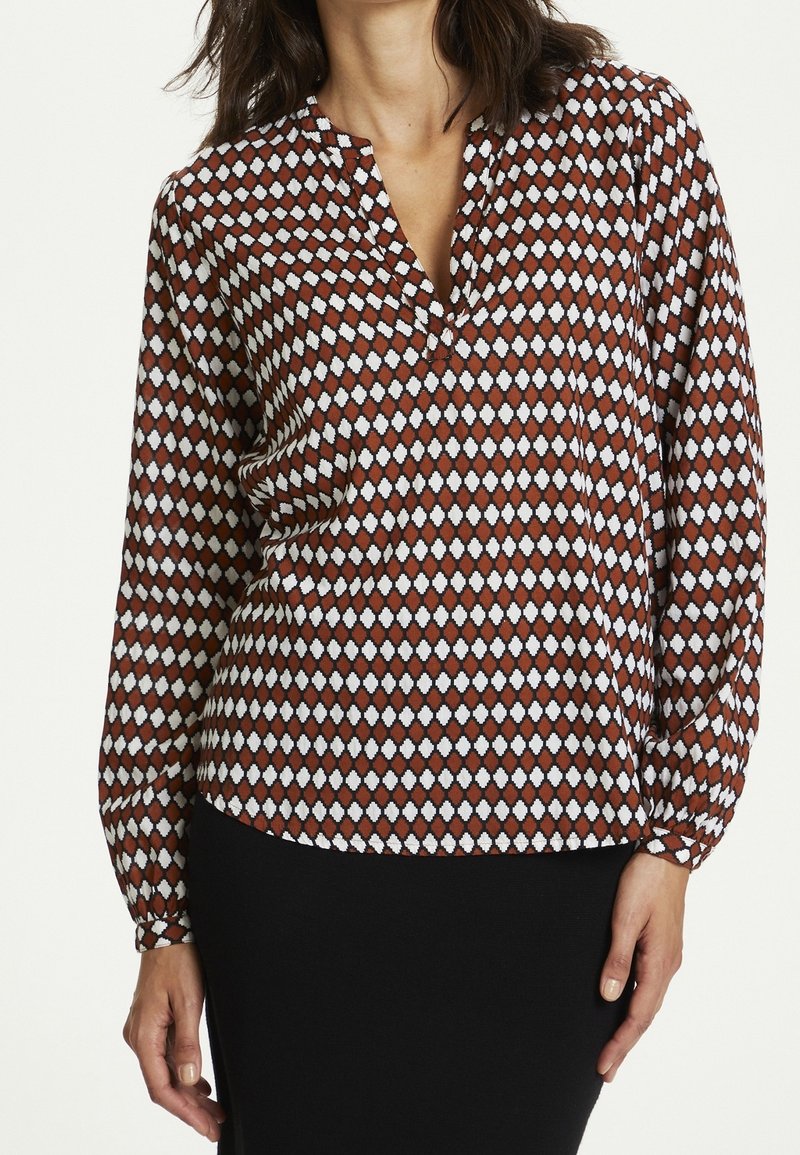 Blusa a maniche lunghe con motivo a rombi rossi e bianchi, dotata di scollatura a V e vestibilità rilassata. Tessuto leggero e morbido con una leggera lucentezza.
