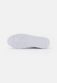 Sole di sneaker bianche con un motivo testurizzato, caratterizzata da scanalature e un logo distintivo. Il materiale in gomma liscia migliora la durata e la presa.