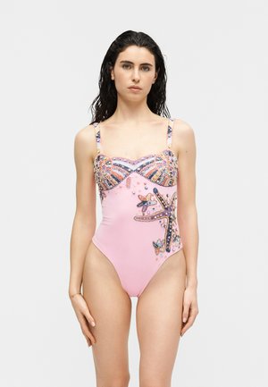 Femeie cu păr lung și închis la culoare poartă un costum de baie roz dintr-o singură piesă, decorat cu scoici și stele de mare colorate, din mărgele.
