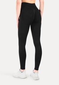 Svarta high-waisted leggings i elastiskt tyg, med en slät yta och en kroppsnära passform, tillsammans med vita träningsskor.