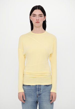 Yellow long-sleeve top with a crew neck, featuring a soft texture and gathered detailing at the waist, paired with light denim jeans.
