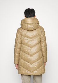 Giacca puffer beige con design a zig-zag, dotata di un ampio cappuccio testurizzato e tasche con zip, realizzata in materiale lucido e leggero.