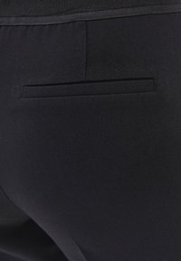 Pantalones negros con un bolsillo trasero plano, textura suave y diseño ajustado para una apariencia elegante.