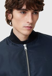 Navy bomber jacket with a zip closure, ribbed collar, and subtle logo detail. Smooth material with a lightweight design.