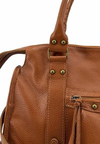 Sac à main en cuir marron avec une surface texturée, des ferrures en laiton, une poche avant zippée et une bandoulière tressée.