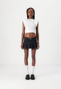 Top corto blanco con mangas acampanadas, combinado con una falda de mezclilla oscura de corte acampanado con bolsillos. Completo con calcetines blancos y zapatos negros.