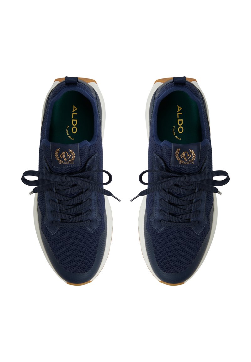 Baskets de sport bleu marine en tissu en maille, à bout arrondi, avec lacets plats et semelle blanche contrastante. Présente un logo doré sur la languette.